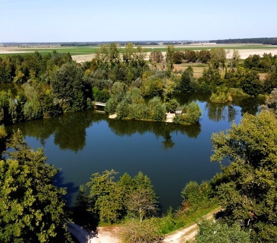 A stunning photo of Juvana taken from a drone showing the lake surrounded by trees with a central island.